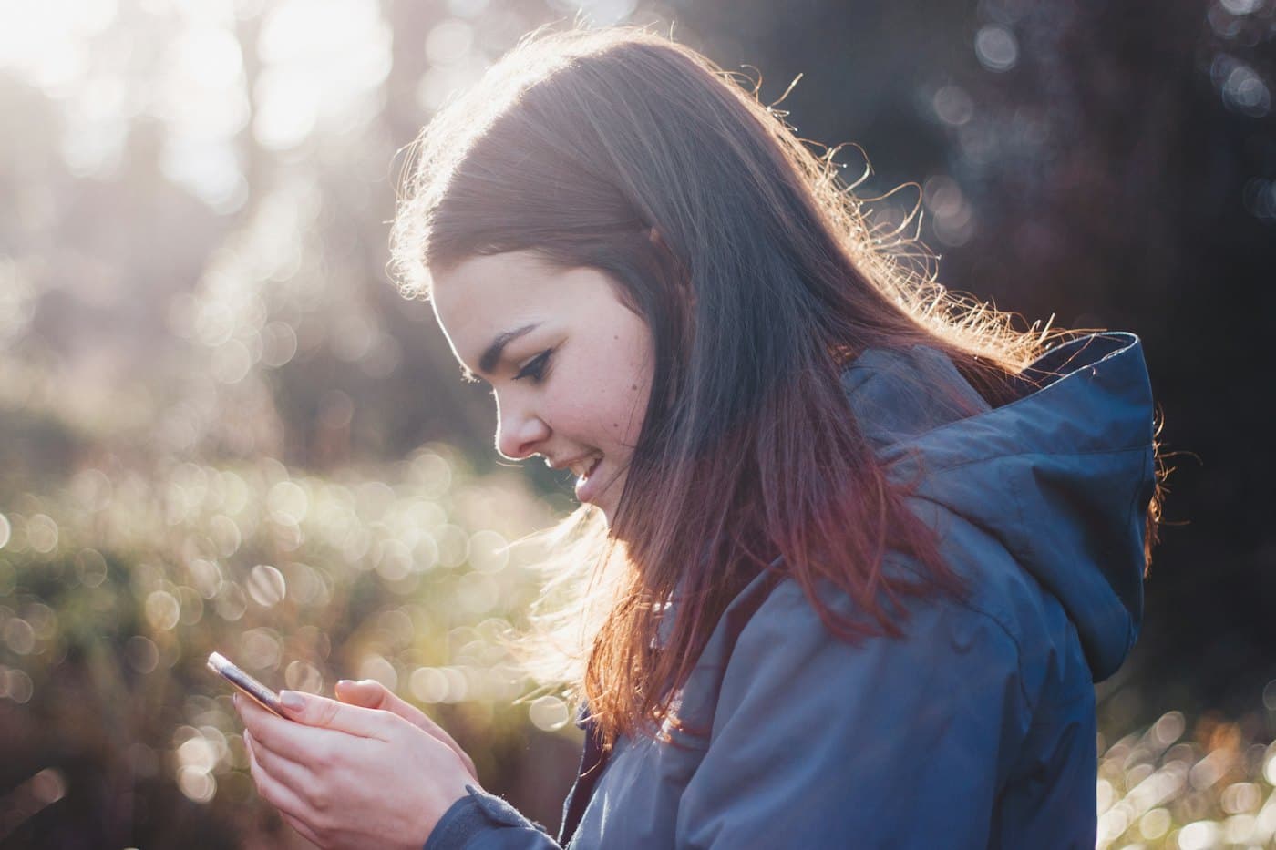 Ung kvinde der bruger sin mobil udenfor i solen
